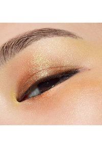 Nahaufnahme eines Auges mit warmen Lidschatten in Goldschimmer, dunklem Eyeliner und einer glatten Hautstruktur rund um das Augenlid.