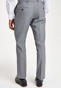 Pantalons gris sur mesure en tissu texturé. Présentent un devant plat, deux poches arrière avec des boutons noirs et une coupe ajustée.