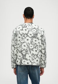 Floral mønstret creme- og grå fleecejakke med dropped shoulders, rund halsudskæring og ribbede kanter, parret med blå denim jeans.