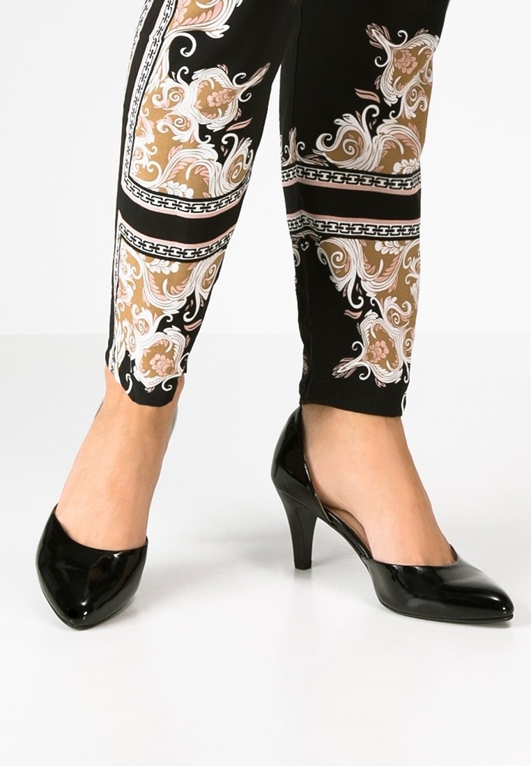 Escarpins en cuir verni noir avec un bout pointu et un talon modeste, associés à un legging noir et doré à motifs représentant des designs floraux.