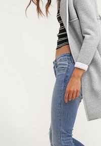 Gray long cardigan over a black and white striped crop top, paired with distressed blue denim jeans. Smooth fabric and casual fit.