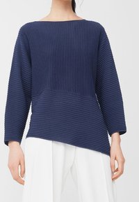 Pull en maille côtelée bleu marine avec un col bateau, des manches longues et un ourlet asymétrique, présentant un tissu texturé et une coupe décontractée.