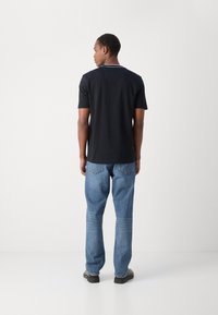 Juodas medvilninis marškinėliai su trumpomis rankovėmis, su apvaliu kaklo iškirpimu su balta apvadu, poruojama su šviesiai mėlynomis džinsais ir tamsiais batais.