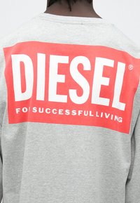 Hall hallipluus, millel on suur punane ristkülikukujuline logo, millel on sõna "DIESEL" valges ning allpool väiksemas valges tekstis "FOR SUCCESSFULLIVING".