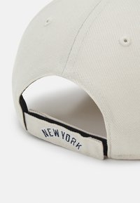 Casquette de baseball beige en tissu texturé, avec "NEW YORK" brodé en noir sur la sangle réglable à l'arrière.