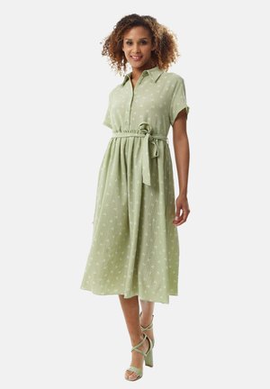 Light green midi dress in textured fabric with a button-up collar, short sleeves, tie waist, and white floral print accents.