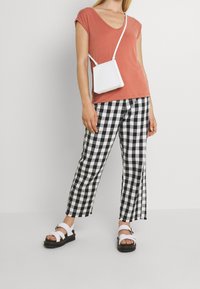 T-shirt a v scollato color ruggine, pantaloni larghi a quadri bianco e nero, borsa a tracolla bianca e sandali bianchi con suola spessa.
