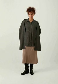 Grey oversized jacket with front pockets, worn over a nude satin skirt and black knee-high boots. Smooth texture, structured design.