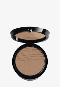 Bronzer compatto in un elegante astuccio nero lucido. Presenta una superficie in polvere pressata con un motivo a onda testurizzato. Il colore è un marrone chiaro con scintillio.