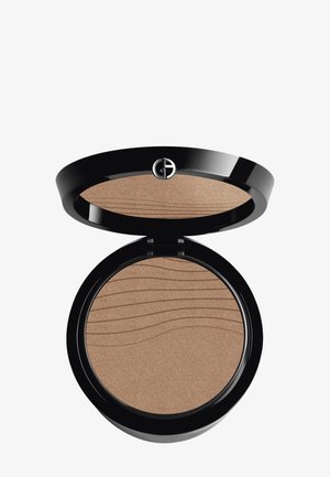 Kompakter Bronzer in einem glänzenden schwarzen Etui. Verfügt über ein strukturiertes Wellenmuster auf der gepressten Puderschicht. Die Farbe ist hellbraun mit Schimmer.