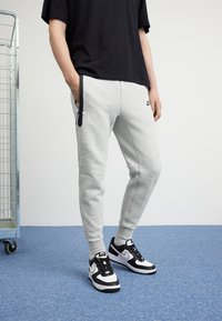 Grå atletiska sweatpants med en smidig design, som har svarta detaljer och en sidoficka, i kombination med svart-vita sneakers.