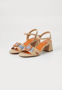 Sandalias de ante beige con una franja de acento azul y hebilla naranja; diseño de dedo abierto, correa en el tobillo y tacón cuadrado.