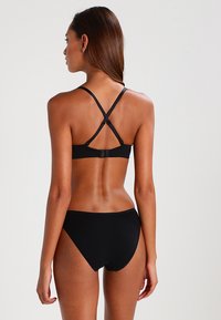 Czarny zestaw bikini z krzyżującymi się ramiączkami i regulowanymi elementami. Miękka, gładka tkanina o minimalistycznym kroju zapewniającym wsparcie.