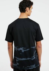 Čierne športové tričko s textúrovanou tkaninou s modrým maskáčovým vzorom v dolnej časti a krátkymi rukávmi. Jednoduchý dizajn s okrúhlym výstrihom.