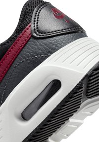 Sneaker en cuir noir avec une accentuation bordeaux, présentant une tige texturée, une semelle intermédiaire blanche et une unité de coussinage d'air visible.