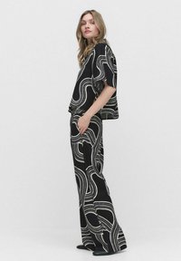 Svart outfit med en löst sittande topp och vida byxor, prydda med vita svängande mönster; mjukt tyg med en avslappnad passform.