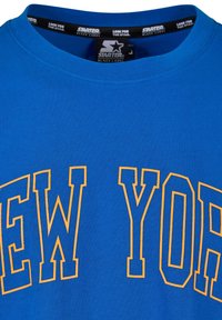 Mėlynas medvilninis marškinėlis, ant kurio raudonai oranžinėmis didžiosiomis raidėmis užrašyta "NEW YORK". Apvalus kaklas ir lygi tekstūra su ryškiu spalvų kontrastu.