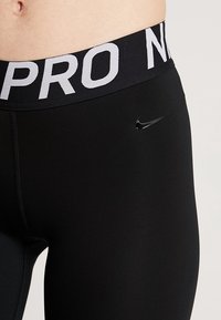 Svarta sportleggings med en bred svart midjeband som har "PRO" i grått. En liten svart Nike-logotyp syns på framsidan.