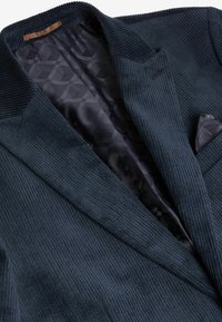 Navy corduroy blazer featuring a textured exterior, notched lapels, and a patterned dark lining. Includes a pocket square.