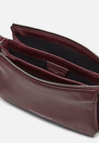 Skórzana torba na ramię w kolorze bordowym z dwiema otwartymi przegrodami, srebrnym zamkiem błyskawicznym i czarną tkaninową podszewką wewnętrzną.