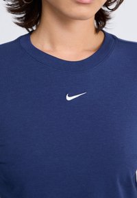 Tamsiai mėlynas medvilninis marškinėlis su apykakle ir trumpomis rankovėmis. Ant krūtinės yra mažas baltas "Nike" logotipas. Lygus paviršius, kasdienis dizainas.