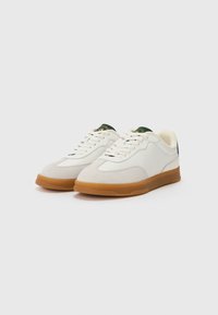 White sneakers with suede and smooth leather upper, round toe, beige rubber sole, and green logo on tongue. Laces in a classic style.