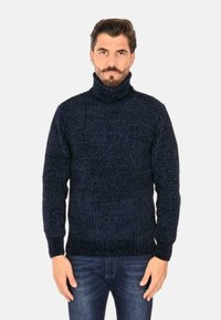 Maglione a collo alto blu navy con texture a coste, maniche lunghe e design aderente. Abbinato a jeans blu scuro.