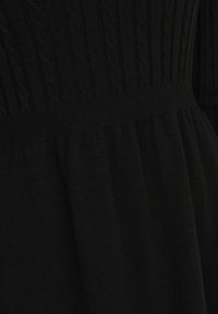 Robe noire en tricot mettant en avant des motifs en relief sur le corsage et une jupe froncée. Texture douce avec une taille cintrée et une partie inférieure fluide.