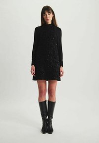 Robe noire à sequins avec une silhouette ajustée et un design sans manches, associée à des bottes noires montantes. Texture lisse et accents brillants.