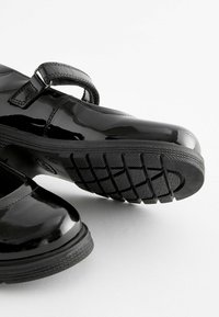 Scarpe in vernice nera con cinturino Mary Jane, dotate di una suola in gomma testurizzata con un motivo antiscivolo e una punta arrotondata.