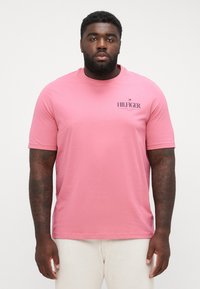 Pink short-sleeve t-shirt made of cotton with a crew neck. Features a small black "HILFIGER" logo on the left side.