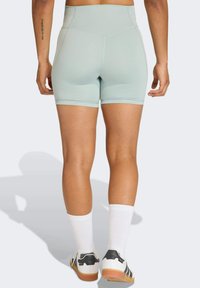 Shorts taille haute bleu clair avec une texture lisse, dotés d'une coupe ajustée et de coutures contrastées. Portés avec des chaussettes blanches et des baskets.