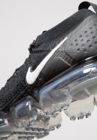 Baskets Nike noires avec une tige en tricot, un logo blanc et une semelle à coussin d'air translucide. Présente un design épuré avec des accents texturés.