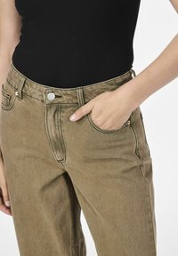Pantalones de mezclilla verde oliva con un corte clásico, que cuentan con cinco bolsillos, un cierre de botón plateado y detalles de costura visibles.