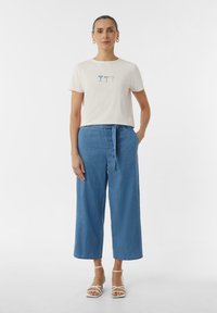 Light pink t-shirt with three cocktail glass designs; paired with blue, loose-fit, high-waisted denim trousers and white strappy sandals.