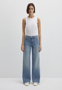 Wide-leg blue denim jeans paired with a fitted white sleeveless top. The jeans feature a high waist and classic five-pocket design.