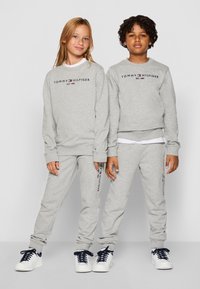 Szürke pulóver és melegítő szett, piros és tengerészkék "Tommy Hilfiger" logóval. A szett fehér sportcipővel kiegészítve.