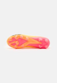 Sole di scarpette da calcio gialle e rosa con tacchetti sagomati, dotata di un design testurizzato e un logo vicino al tallone per una maggiore trazione.