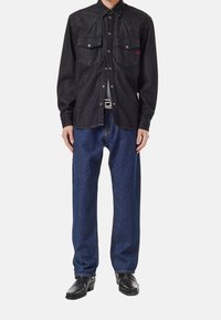 Svart denimskjorta med spetsig yoke, två bröstfickor och tryckknappar; kombinerad med lösa blåjeans och svarta ankelskor.