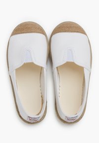 Baskets blanches en toile sans lacets avec une semelle en caoutchouc beige texturée et un bout arrondi. Présentent un panneau élastique central pour un enfilage facile.