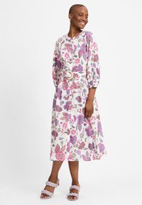 Blumiges Midikleid mit rosa und blauen Mustern auf hellem Hintergrund, mit puffärmel und einem Gürtel. Kombiniert mit lavendelfarbenen geflochtenen Absätzen.