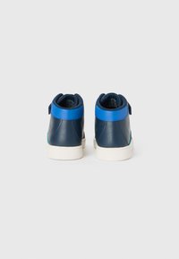 Een paar marineblauwe en witte hoge sneakers met felblauwe hielaccenten, gezien vanaf de achterkant op een effen witte achtergrond.