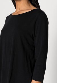 Sort, langærmet top lavet af blødt bomuld; har en bred, scoop halsudskæring og en afslappet pasform med en glat tekstur.