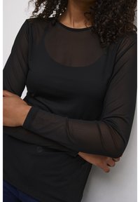 Haut noir à manches longues en matière transparente avec un col arrondi et une texture lisse, présentant une couture apparente et un détail de logo subtil.