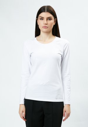 Chemise blanche à manches longues en tissu doux, avec un col rond et une coupe slim. Comprend un logo discret au niveau de l'ourlet.