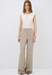 Beige leveled-leg trousers with a textured finish, paired with a cream top featuring a keyhole detail and gold embellishments at the neckline.