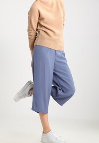 Pantaloni a gamba larga blu chiaro realizzati in tessuto morbido, con una vestibilità rilassata e orli risvoltati, abbinati a sneakers bianche e un maglione beige.