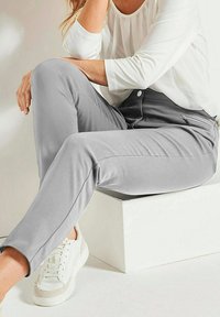 Lichtgrijze gepaste broek gemaakt van een zachte stof, met een ritszak, gecombineerd met een witte lange mouw top en witte sneakers.