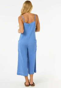 Mono de algodón azul con tirantes de espagueti, corte holgado, piernas cortas y dos bolsillos laterales. Tejido texturizado con un aspecto suave y transpirable.