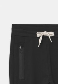 Zwarte joggingbroek met een trekkoordsluiting en een getextureerde ritszak aan de zijkant; zachte stof met een gladde afwerking.